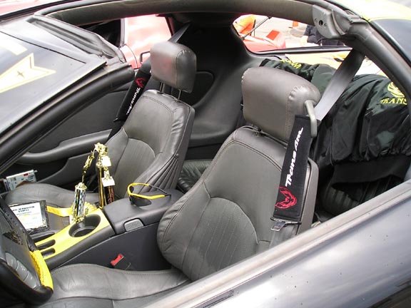 Interior of a 1994 Pontiac Trans Am with grey leather seats, trophies on the console, and a jacket on the passenger seat