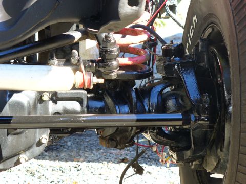 1978 Ford Bronco - Close-up under a lifted 4x4 looking along a freshly painted black solid front axle, showing the knuckle, ball joints, tie rod with red-oran…