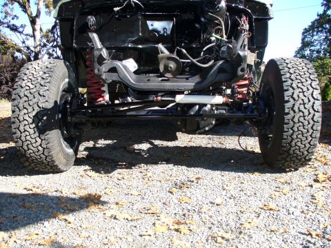 1978 Ford Bronco - Head-on low view under a 4x4 with the front sheetmetal removed, showing the freshly painted black solid front axle, coil springs, radius ar…