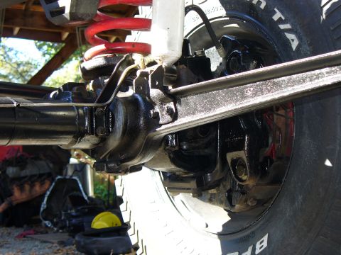1978 Ford Bronco - Tight low view of a black-painted solid front axle showing the knuckle, ball joints, tie rod and drag link, disc brake caliper and rotor be…