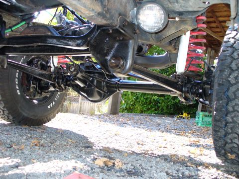1978 Ford Bronco - Ground-level view under a lifted 4x4 along the fresh black-painted front axle, differential and radius arms, with the tie rod, drag link, r…