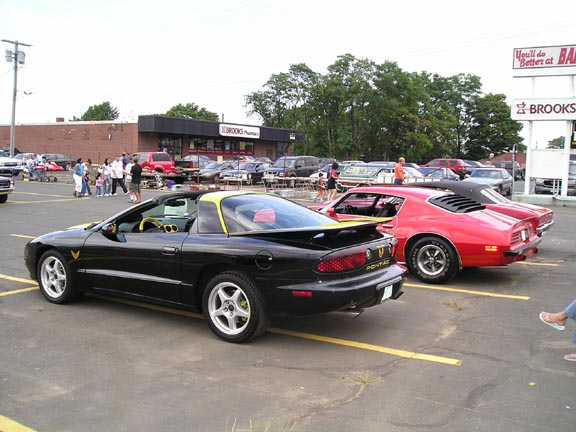 Black 1994 Pontiac Trans Am with yellow T-tops and interior accents, parked next to a red car