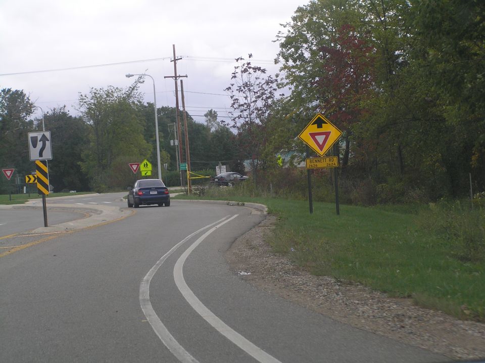 Blue sedan driving on a road with yield signs and a school crossing sign