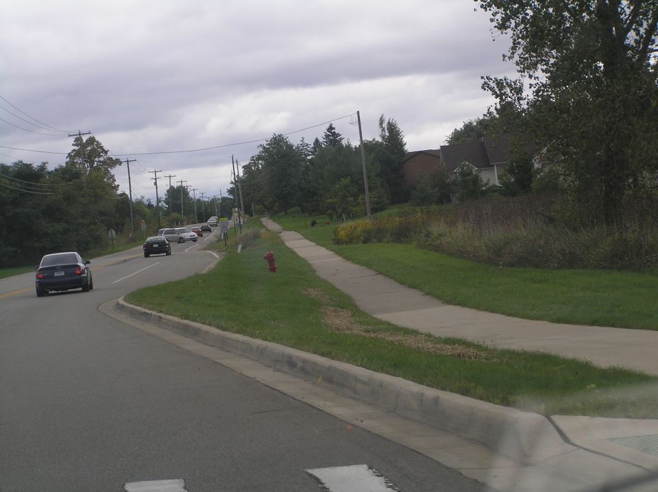 Dark sedan driving on a road with other cars and houses in the background