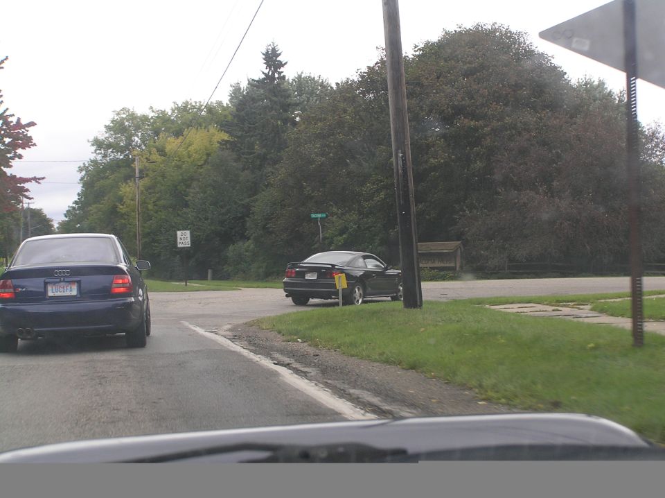Dark sedan and black coupe on a tree-lined road
