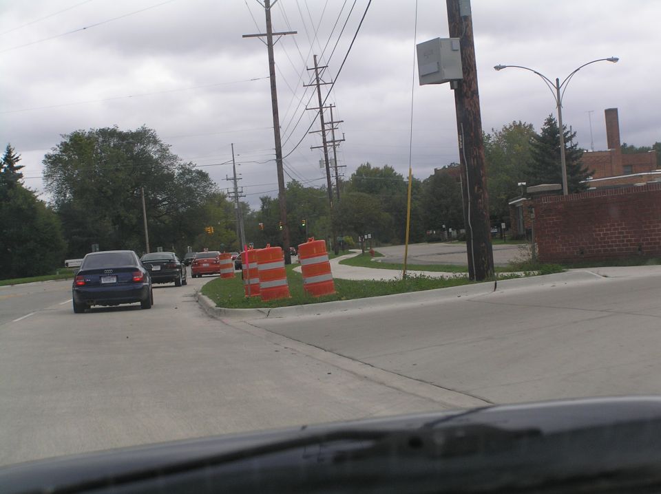 View through windshield of dark blue Audi sedan ahead on a road with orange construction barrels