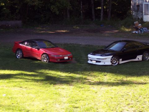 1996 Ford Probe - Two sports coupes, one red and one black with a white body kit, are parked on a lawn.