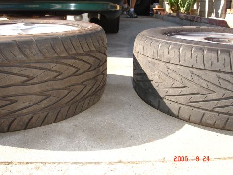 1993 Ford Taurus - A close-up view of two tires and their rims, with a portion of a green vehicle in the background.