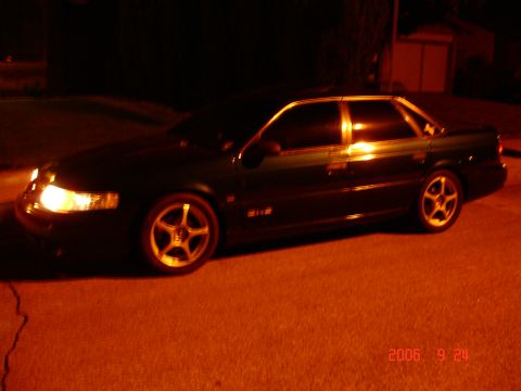 1993 Ford Taurus - A dark sedan is parked on a street at night, illuminated by streetlights and its own headlights.