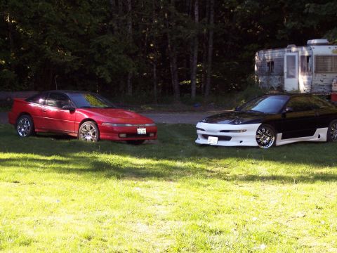 1996 Ford Probe - Two sports cars, a red one and a black and white one, are parked on a grassy area near a trailer.
