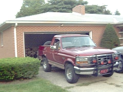1994 Ford Bronco - Red Ford pickup truck with a brush guard parked in front of a brick garage.