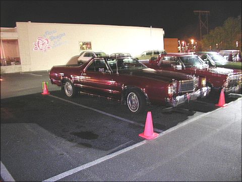 1967 Ford Ranchero - A line of vehicles, including a maroon Ford Ranchero, are parked in a lot under artificial lighting at night.