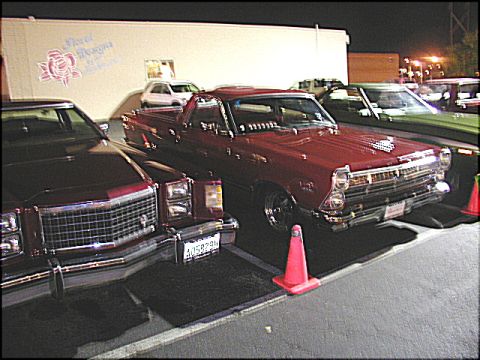1967 Ford Ranchero - A red pickup truck is parked in front of a building with floral designs, alongside other vehicles.