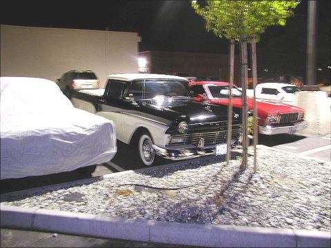 1967 Ford Ranchero - A vintage black and white pickup truck is parked in a lot at night, with other vehicles nearby.