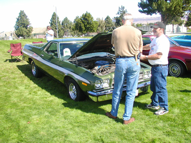 Green 1970s Ranchero with hood up showing blue V8 at a grass car show