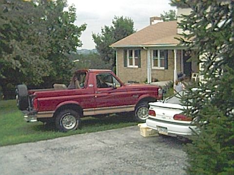 1994 Ford Bronco - A red Ford Bronco is parked on the grass beside a house, with a white car in the driveway.