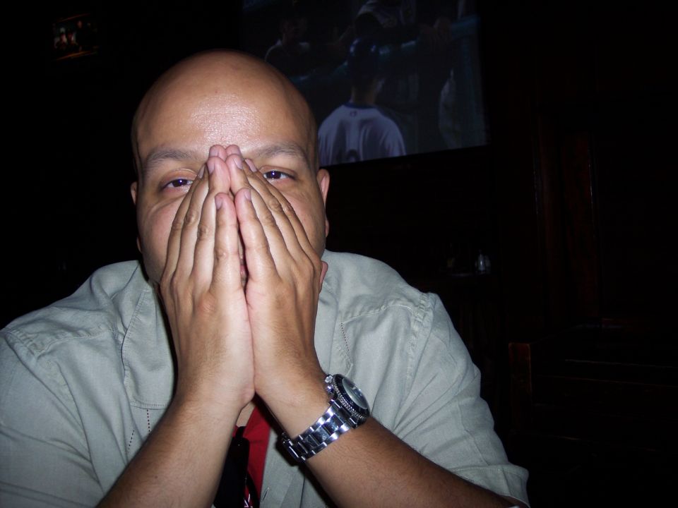 man with hands over face, wearing a watch, with a screen showing a game in the background