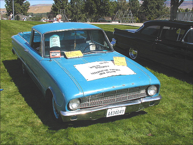 Light blue early-1960s Ford Falcon Ranchero pickup with show placards on grass