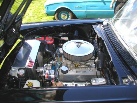 1967 Ford Ranchero - The engine compartment of a black classic car is shown, with another blue vehicle visible behind it.