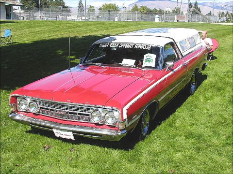 1967 Ford Ranchero - A red 1967 Ford Ranchero pickup is displayed on a grassy field with a camper shell on the bed.