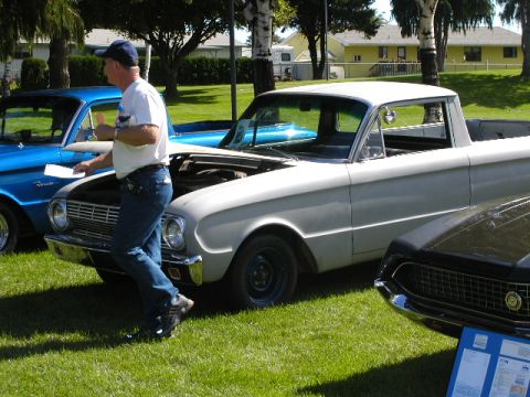 1967 Ford Ranchero - A man walks past a light-colored 1960 Ford Falcon Ranchero at an outdoor car show.