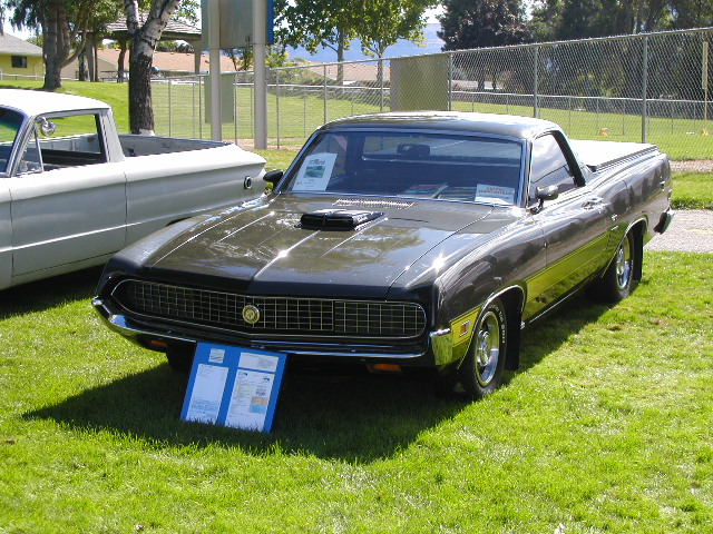 Dark bronze Ford Ranchero with hood scoop at a grass car show, front 3/4 view