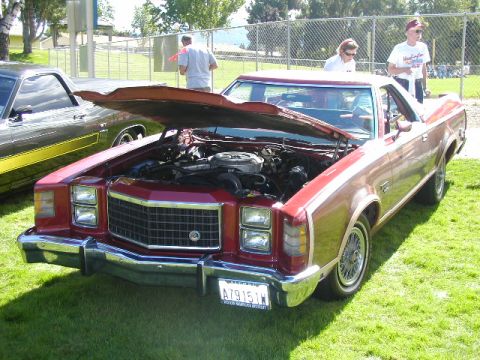 1967 Ford Ranchero - This red Ford Ranchero, likely a 1977 model, is displayed with its hood open, revealing the engine compartment. Another vehicle is parked a…
