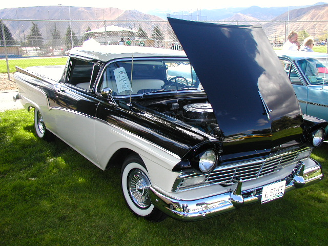 Black and white 1957 Ford Ranchero at car show with hood open on grass