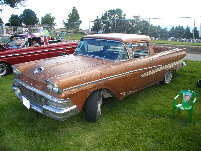 Bronze vintage Ford Ranchero car-pickup with patina, lowered stance, parked on show grass.
