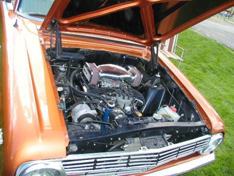 1967 Ford Ranchero - The engine bay of an orange 1967 Ford Ranchero is open, revealing a V8 engine with chrome air cleaners.