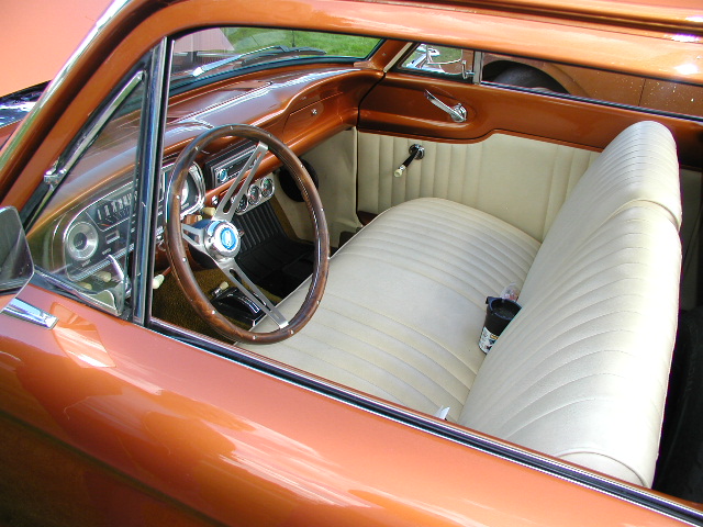 Interior of a classic car with wood-rimmed steering wheel, bench seat, and dashboard gauges