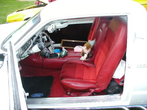 1967 Ford Ranchero - The interior of a 1967 Ford Ranchero shows red seats and a custom steering wheel, with a yellow vehicle visible outside.