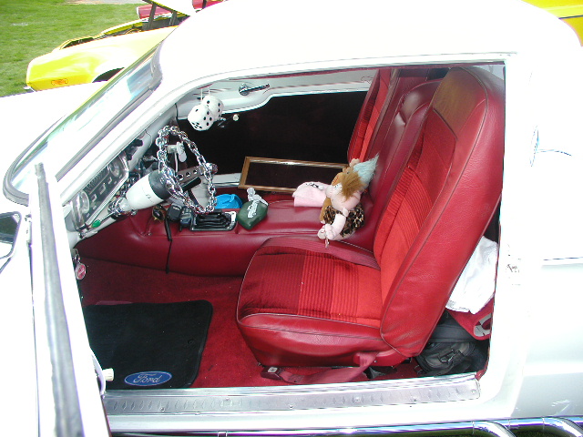 Red vinyl interior of white classic Ford with chain steering wheel and Ford floor mat, seen through door