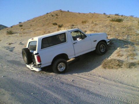 1996 Ford Bronco - A white Ford Bronco navigates a sandy, off-road trail under a clear blue sky.