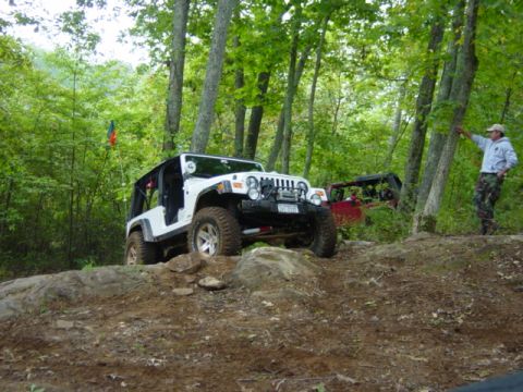 1991 Ford Bronco - A white Jeep Wrangler tackles an off-road obstacle, with another Jeep visible behind it in a wooded area.