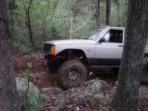 1991 Ford Bronco - This Jeep Cherokee is off-roading on a rocky trail surrounded by trees.