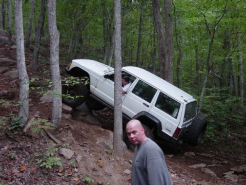 1991 Ford Bronco - A white Jeep Cherokee navigates a challenging off-road course through a dense forest.