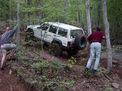 1991 Ford Bronco - A white Jeep Cherokee XJ navigates a challenging off-road trail in a forest setting.