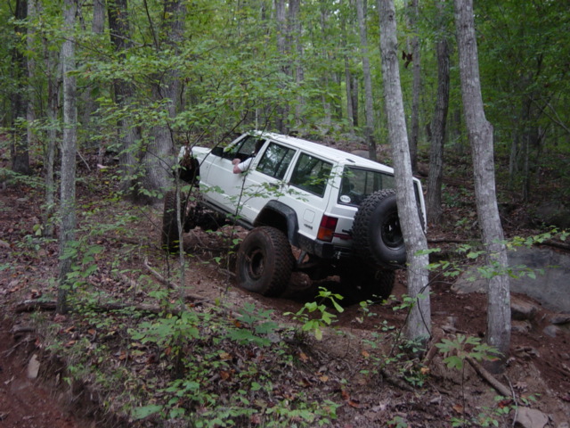 White Jeep Cherokee climbing a steep, wooded trail with large tires