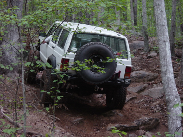 White Jeep Cherokee XJ on a rocky, wooded trail, rear view