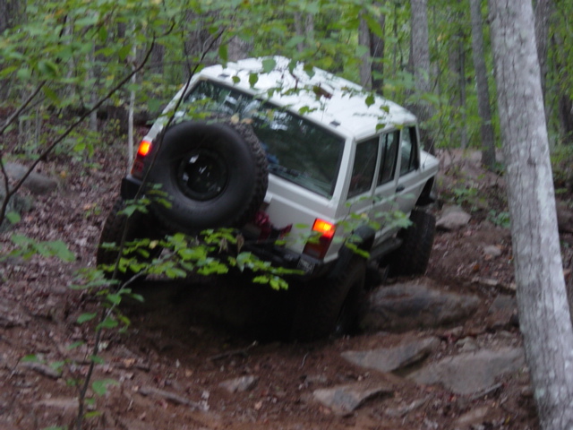 White Jeep Cherokee XJ climbing over rocks on a wooded trail