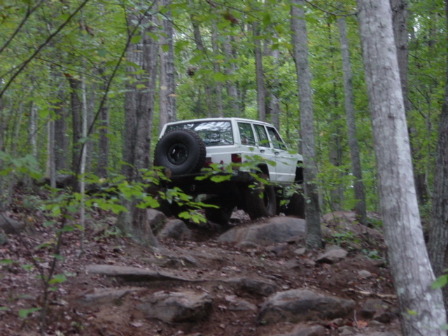 White SUV with spare tire on rear, navigating a rocky forest trail