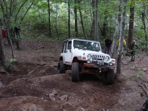 1991 Ford Bronco - A white Jeep Wrangler navigates a challenging off-road trail through a forest.