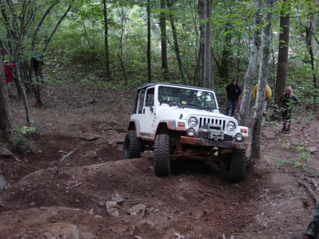 White Jeep Wrangler TJ model driving on a muddy, wooded trail