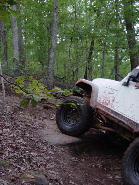 1991 Ford Bronco - A white jeep is shown navigating a challenging off-road trail through a wooded area.