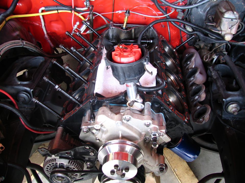 Partially assembled V8 engine in bay with exposed cylinders, red distributor cap, and polished pulley