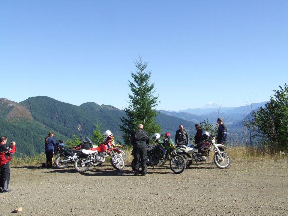 Group of motorcycles and riders on a dirt road with mountains in the background