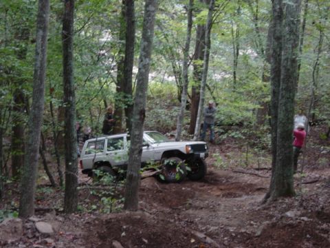 1991 Ford Bronco - A white Jeep Cherokee XJ navigates a challenging off-road trail through a wooded area.