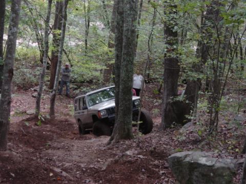 1991 Ford Bronco - A Jeep Cherokee navigates a challenging off-road trail through a forest.