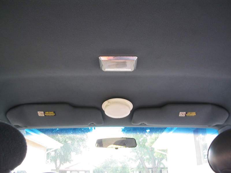 Car interior ceiling with two sun visors, a dome light, and a rectangular interior light. Air bag warning labels are visible on the visors